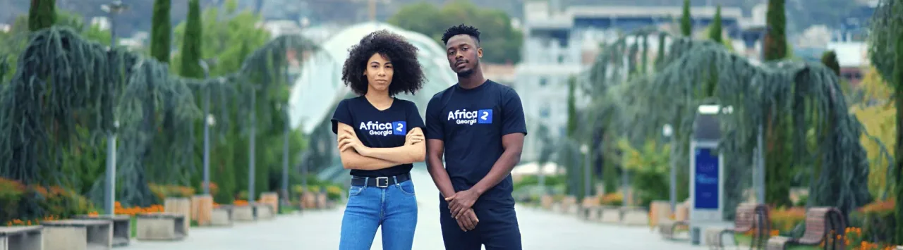 Two people wearing Africa2Georgia T-shirts beside a park fountain